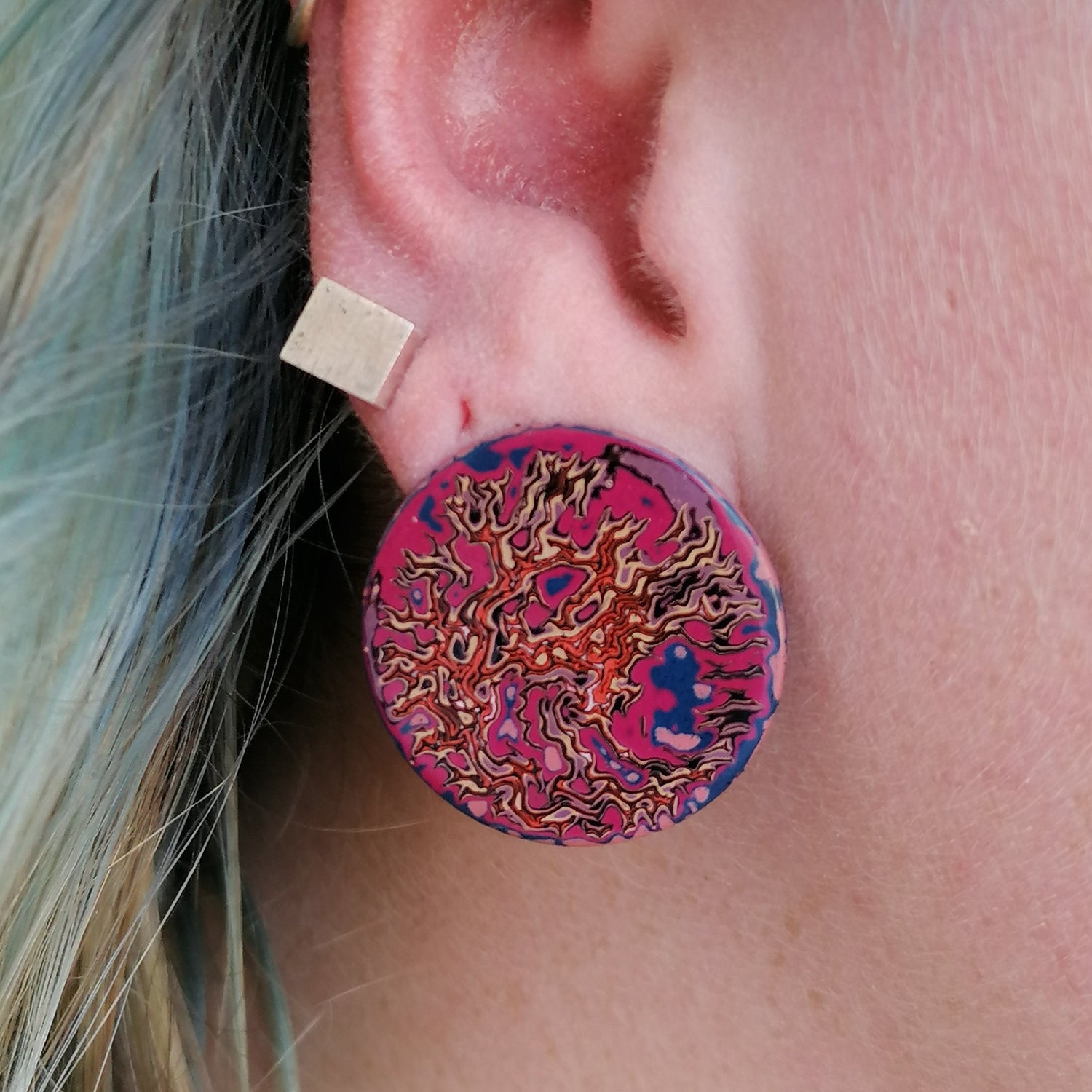 Image is focused in on the ear and  shows  a single earring, wrinkled pattern in orange yellow pink and blue