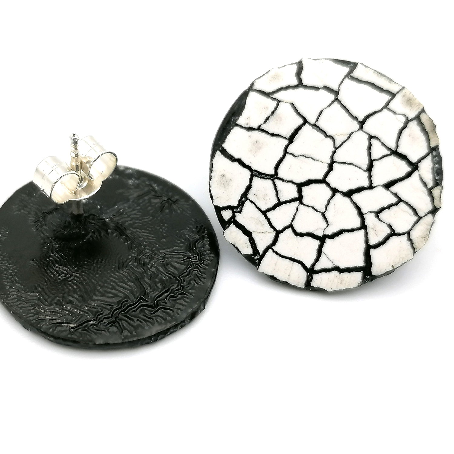 Image shows two round stud modern mosaic earrings made using the Rankaku technique using real eggshell, white on black. One earring is upside down showing the sterling silver earring post