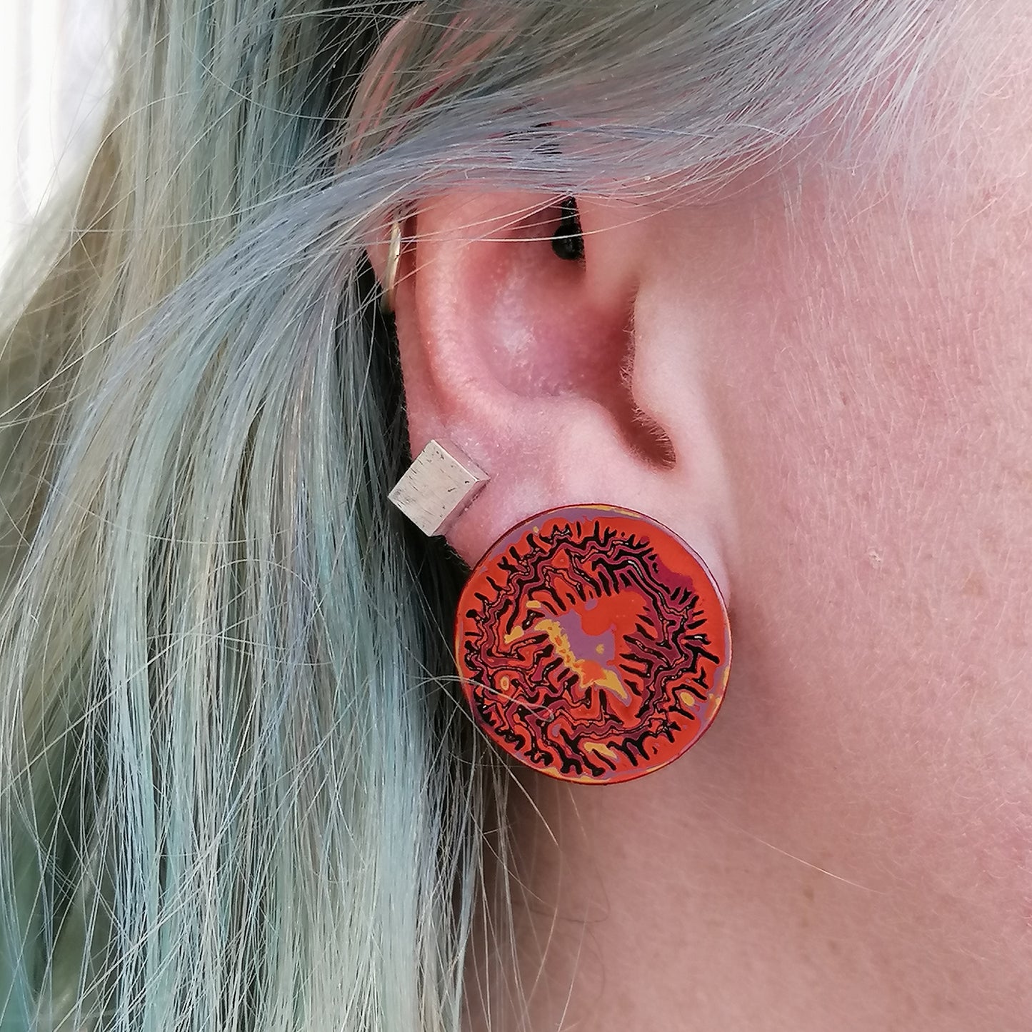 Image shows a single earring being worn by a model with blue hair. Shiney and slick with a wrinkled pattern in orange, pink, yellow and liliac