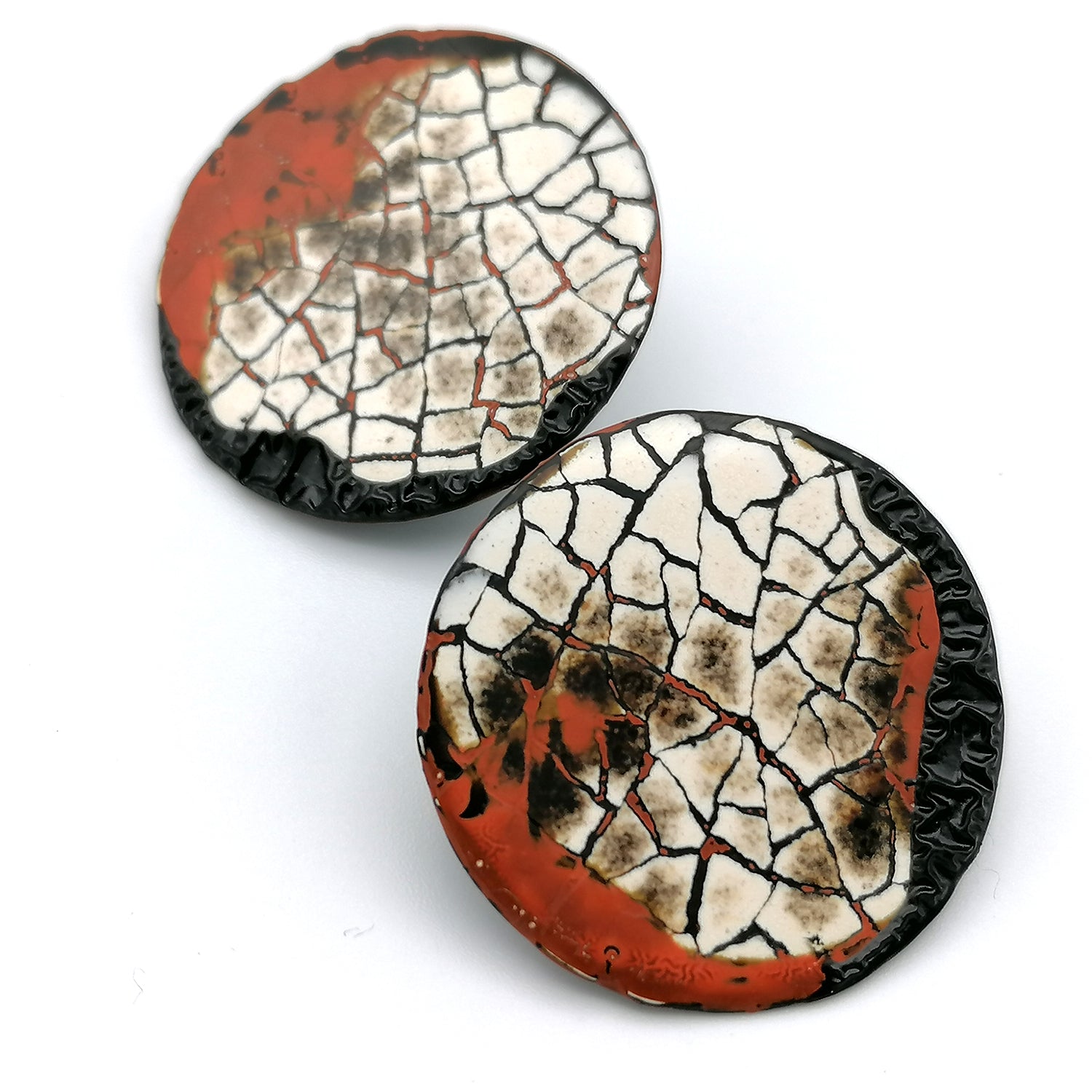 Images shows a pair of round stud earrings on a white background. Modern mosaic earrings made out of real eggshell and black lacquer with an area of raised black wrinkled texture and patches of red.