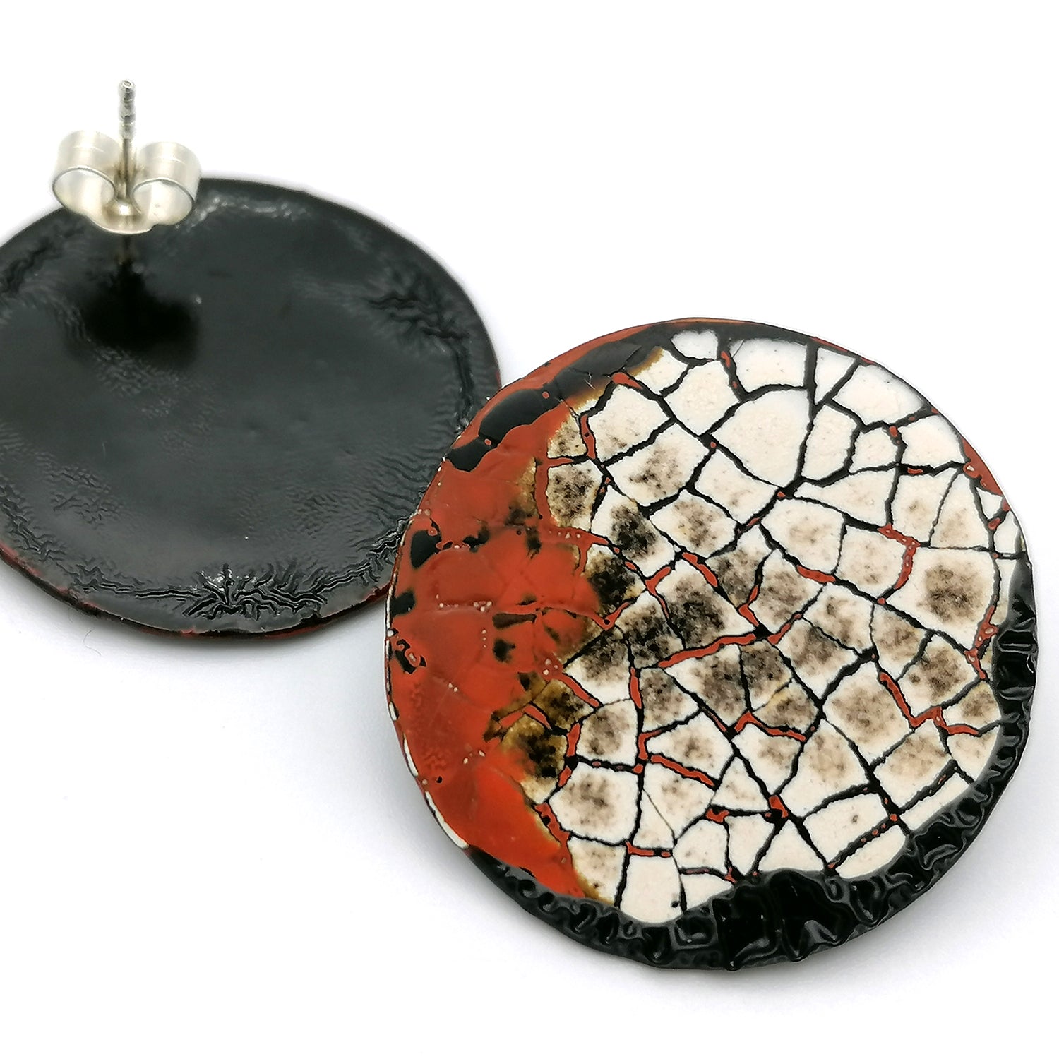 Images shows a single round stud earring, one is upside down showing the sterling silver earring post.. Modern mosaic earrings made out of real eggshell and black lacquer with an area of raised black wrinkled texture and patches of red.