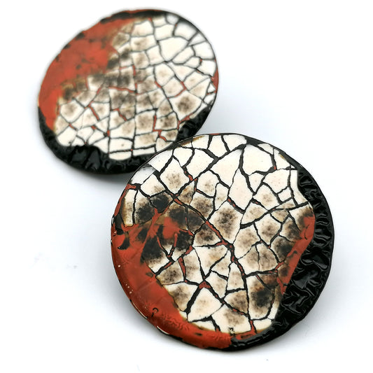 Images shows a pair of round stud earrings on a white background. Modern mosaic earrings made out of real eggshell and black lacquer with an area of raised black wrinkled texture and patches of red.